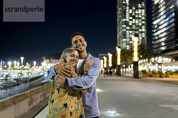 Lächelnder Mann umarmt Freundin nachts in der Stadt