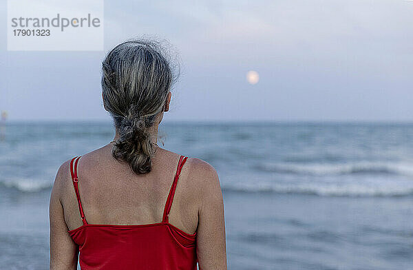 Frau mit grauem Haar blickt auf den Mond über dem Horizont