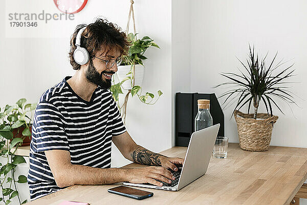 Freiberufler mit kabellosen Kopfhörern arbeitet im Heimbüro am Laptop