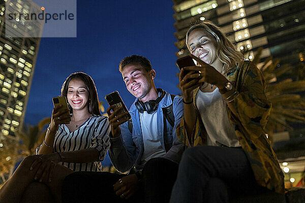 Fröhliche junge Männer und Frauen surfen nachts über Smartphones im Internet