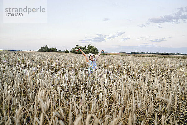 Happy girl with arms raised amidst crops in farm