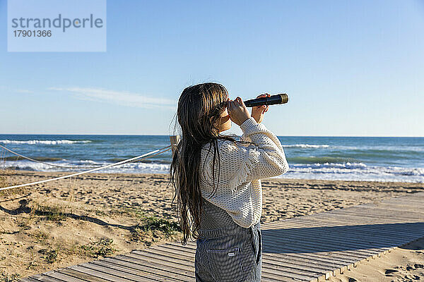 Mädchen beobachtet das Meer an einem sonnigen Tag durch ein Monokular
