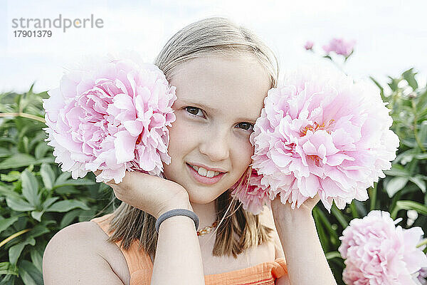 Lächelndes blondes Mädchen mit rosa Pfingstrosenblüten