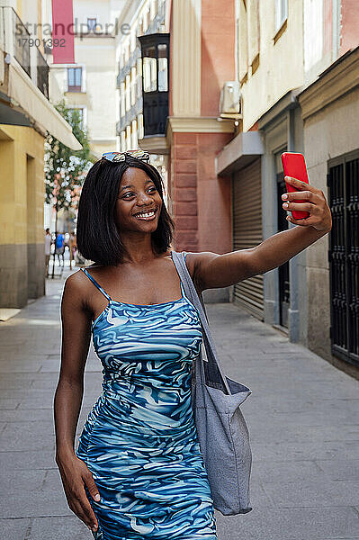 Lächelnde junge Frau  die unterwegs ein Selfie mit dem Smartphone macht