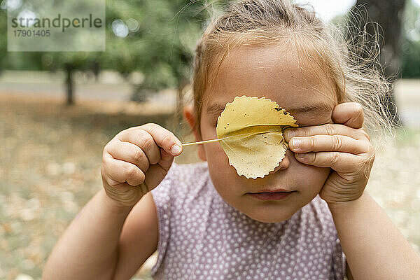 Girl covering eyes with leaf at public park