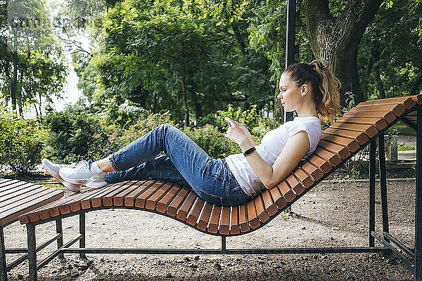 Frau benutzt Mobiltelefon und entspannt sich auf Liegestuhl im Park