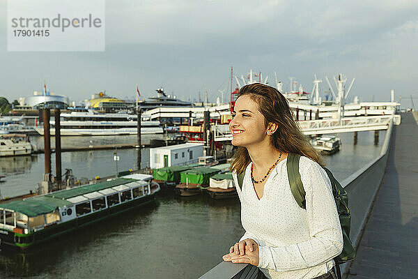 Glückliche Frau steht an einem sonnigen Tag am Geländer im Hamburger Hafen