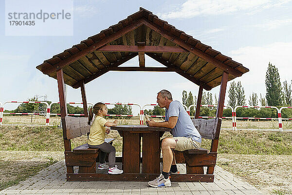 Reifer Mann und Mädchen essen am hölzernen Picknicktisch auf dem Parkplatz