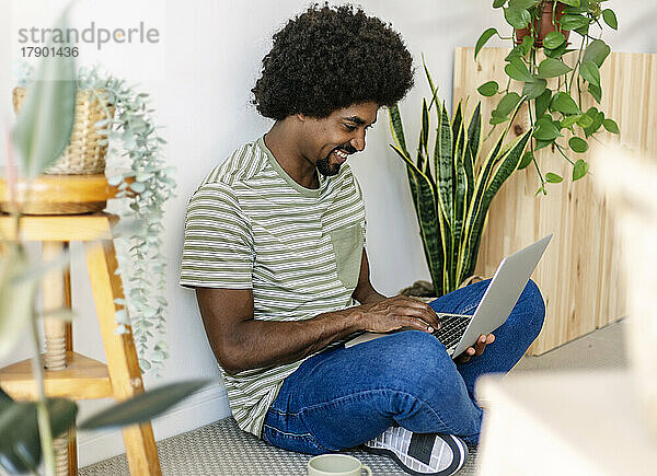 Glücklicher afrikanischer Mann  der zu Hause einen Laptop benutzt