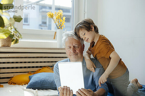 Älterer Mann macht Selfie mit Enkel über Tablet-PC im Wohnzimmer