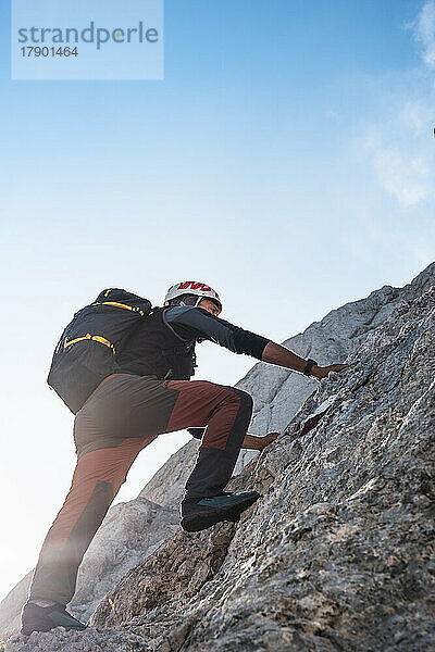 Bergsteiger klettert an einer Felswand unter blauem Himmel