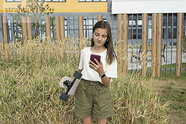 Lächelndes Mädchen mit Smartphone  das vor Gras steht
