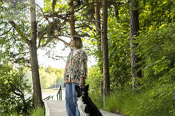 Nachdenkliche junge Frau steht neben Hund im Park