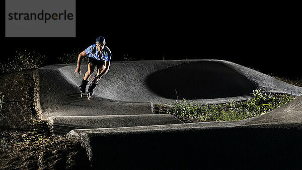 Junger Mann übt nachts Inlineskaten im Skateboardpark