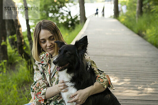 Junge Frau sitzt mit Hund an der Promenade im Park