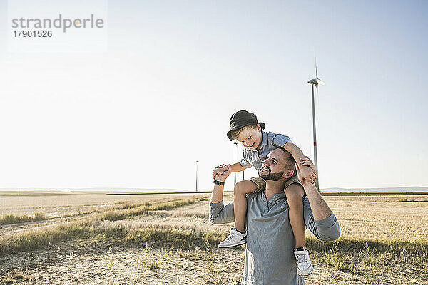 Vater trägt Sohn auf Schultern vor Windkraftanlagen