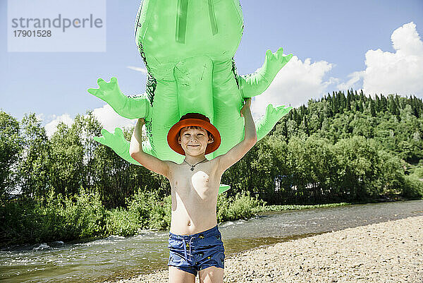 Lächelnder Junge hält an einem sonnigen Tag ein aufblasbares Krokodil