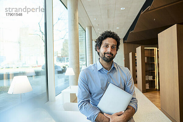 Lächelnder Mann mit Laptop in der Bibliothek