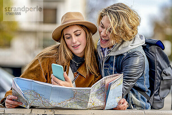Mann teilt Smartphone mit Frau  die im Urlaub eine Karte hält