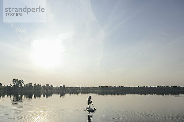 Frau macht Standup-Paddleboarding im See unter freiem Himmel