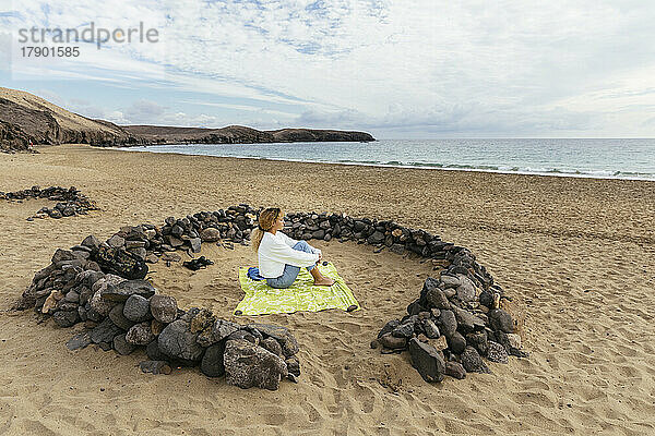 Junge Frau sitzt inmitten von Felsen und blickt vom Strand aus auf das Meer