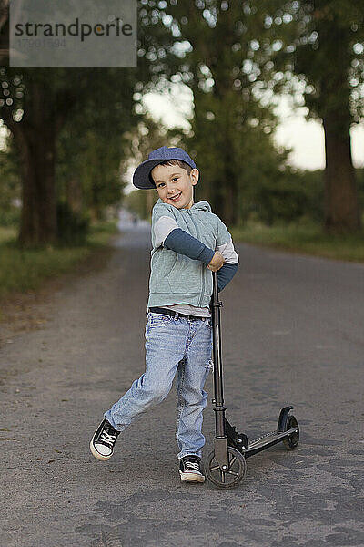 Smiling boy with push scooter on footpath