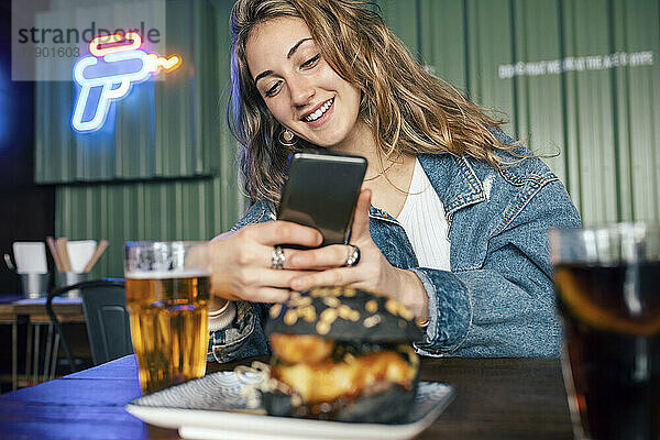 Glückliche Frau fotografiert Essen per Smartphone im Restaurant