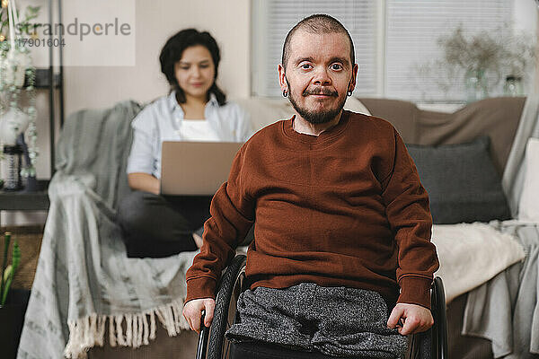 Lächelnder Mann im Rollstuhl vor Freundin mit Laptop zu Hause