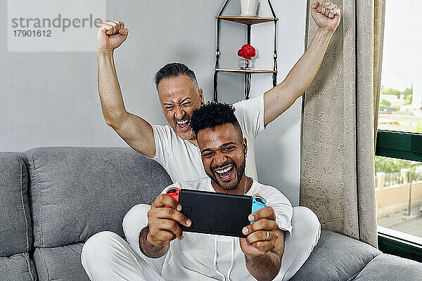 Reifer Mann jubelt seinem Freund zu  der zu Hause ein Videospiel spielt