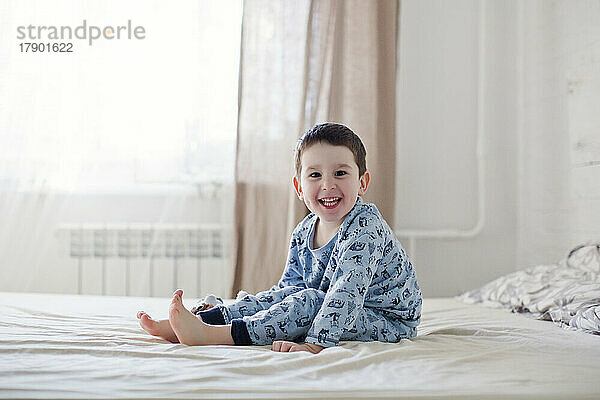 Glücklicher süßer Junge im Pyjama  der auf dem Bett sitzt