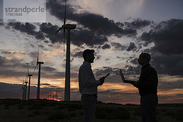 Ingenieure diskutieren bei Sonnenuntergang mit Laptop im Windpark