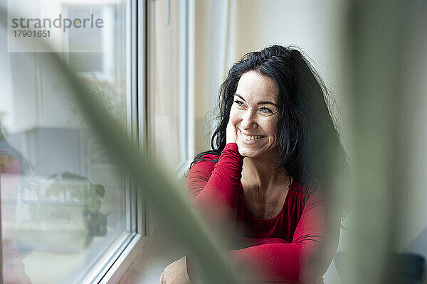 Lächelnde brünette Frau  die durch das Fenster schaut