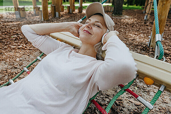 Reife Frau hört Musik und entspannt sich in der Hängematte im Park