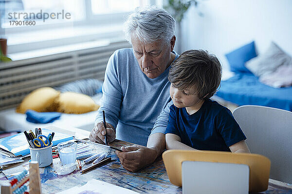 Älterer Mann zeichnet zu Hause auf Tablet-PC von Enkel