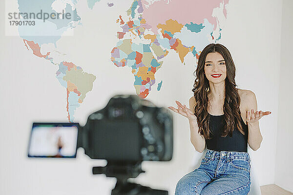 Happy young influencer filming in front of world map on wall