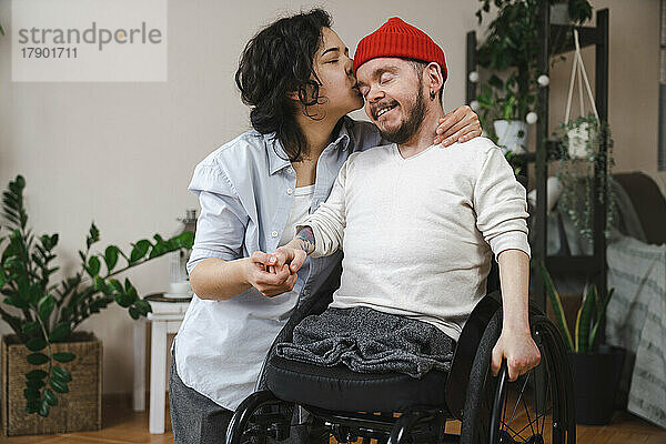 Frau küsst Freund mit Behinderung zu Hause auf den Kopf