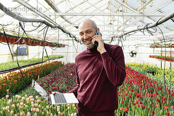 Glückliche Geschäftsfrau telefoniert mit Laptop im Tulpengewächshaus