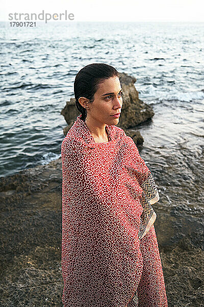 Nachdenkliche Frau  in eine Decke gehüllt  steht am Ufer