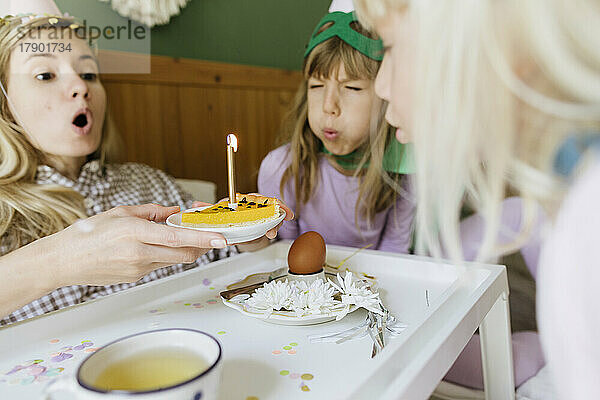 Mutter und Töchter blasen gemeinsam Kerze auf Kuchen