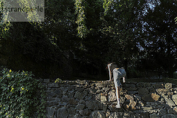 Nicht-binäre Person klettert auf Steinmauer