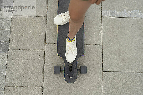 Mädchen steht auf Skateboard am Fußweg