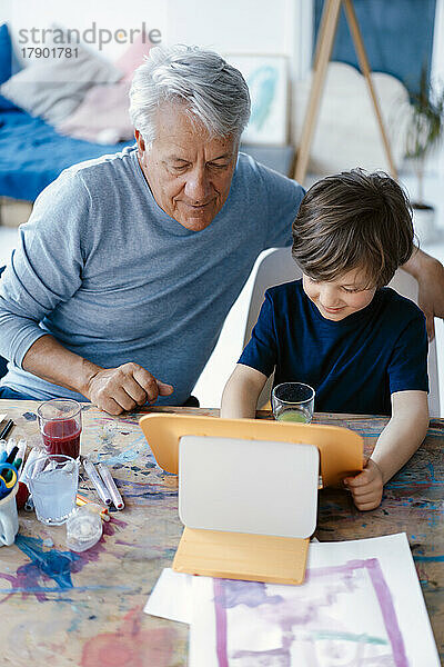 Lächelnder Junge benutzt Tablet-Computer von Großvater zu Hause