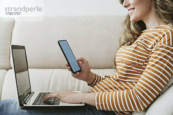 Frau benutzt Laptop und Mobiltelefon auf dem Sofa