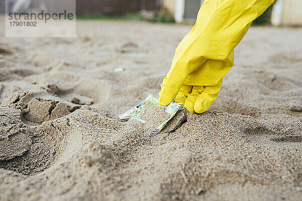 Hand einer Frau  die am Strand Müll vom Sand aufsammelt