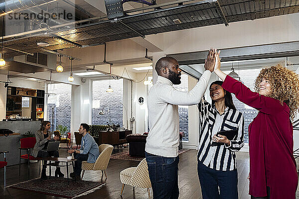 Junge Geschäftsfrauen und Kollegen feiern im Büro High-Five