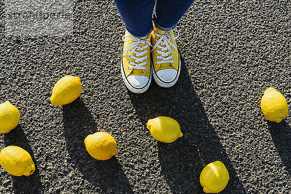 Frau in Segeltuchschuhen steht neben Zitronen auf Asphalt