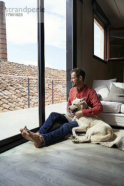 Nachdenklicher Mann sitzt mit Hund und schaut durchs Fenster