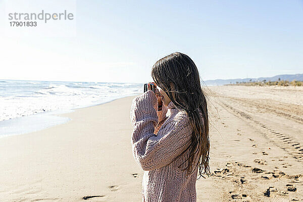 Mädchen klickt am Strand auf Fotos von der Kamera