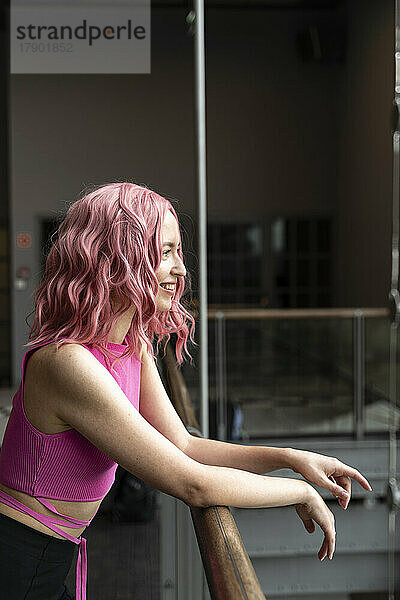 Smiling woman with pink hair standing by railing