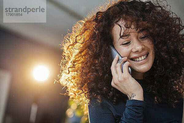 Glückliche schöne Frau mit lockigem Haar  die mit dem Handy spricht